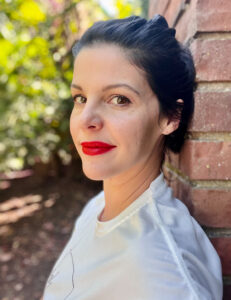 Laura Page leaning against a brick wall with the woods in background.